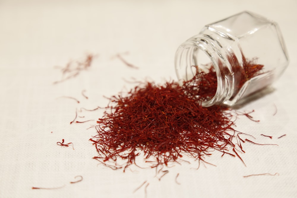 Grade-1 pushal saffron threads spilling from a small glass jar onto cream linen