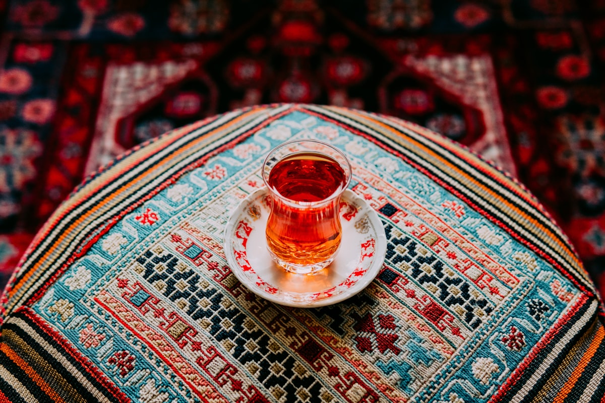 A glass of amber Persian tea on a patterned woven cushion and carpet
